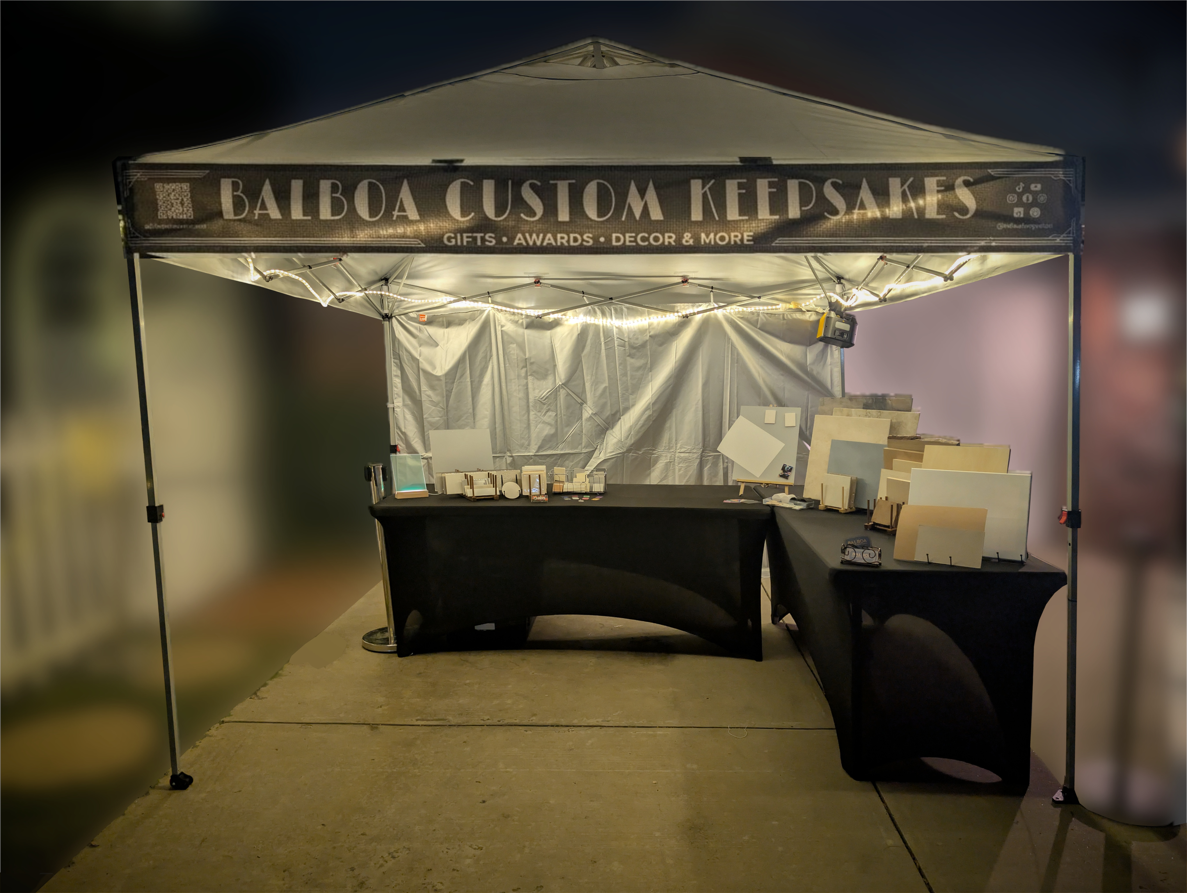 Balboa Custom Keepsakes booth at night, lit warmly under canopy lights